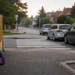 Přechod u školy, zaparkovaná auta a školní batoh u plotu.